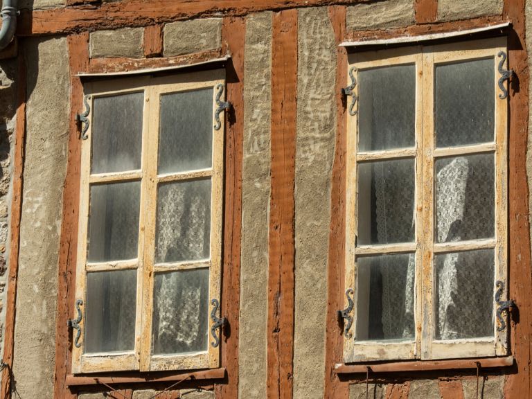 Zwei alte Holzfenster mit abblätterndem Anstrich in einer Backsteinfassade